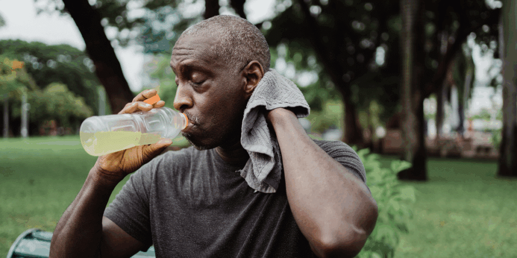 A tired man having energy drink while wiping his sweat with towel.