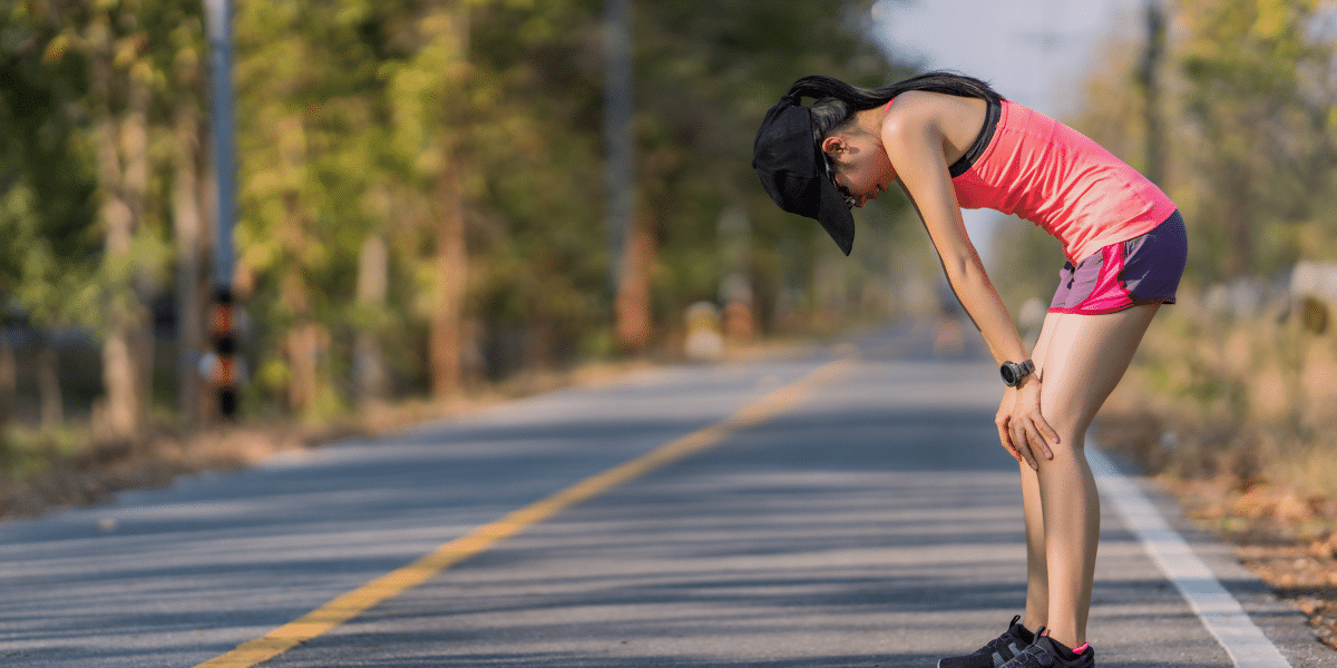 Exhausted runner pausing on roadside in workout gear.