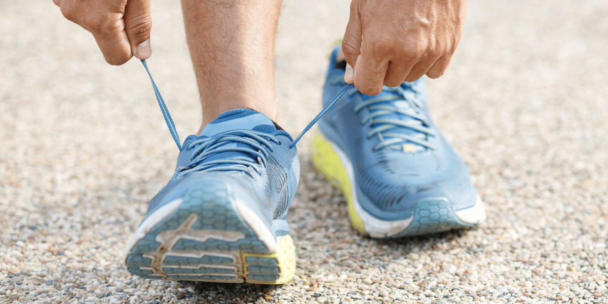 Person tying running shoe on track at sunset.