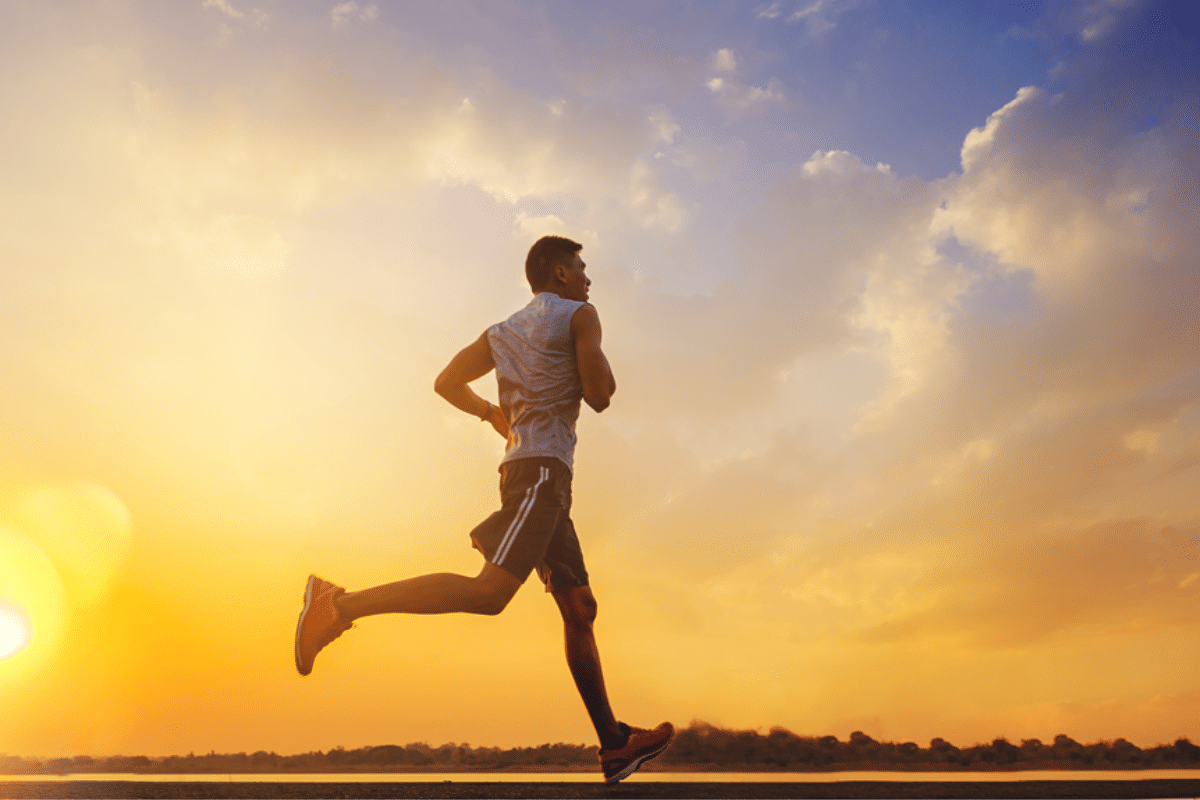 Man running at sunrise with colorful sky backdrop.