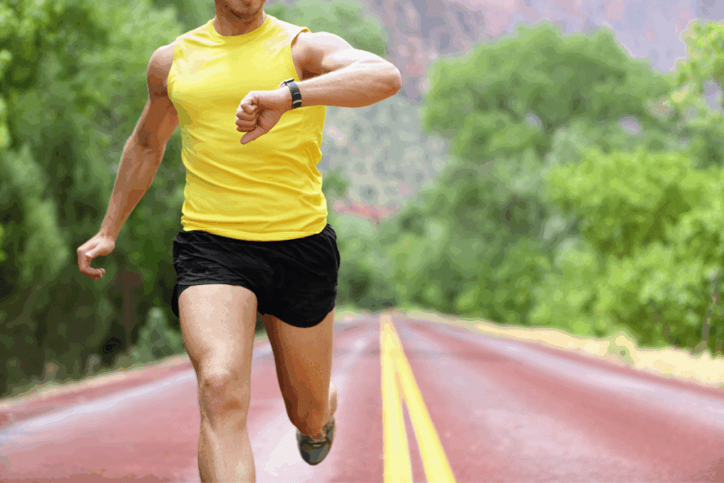 A man wearing yellow vest and looking at his watch while running.
