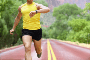 A man wearing yellow vest and looking at his watch while running.