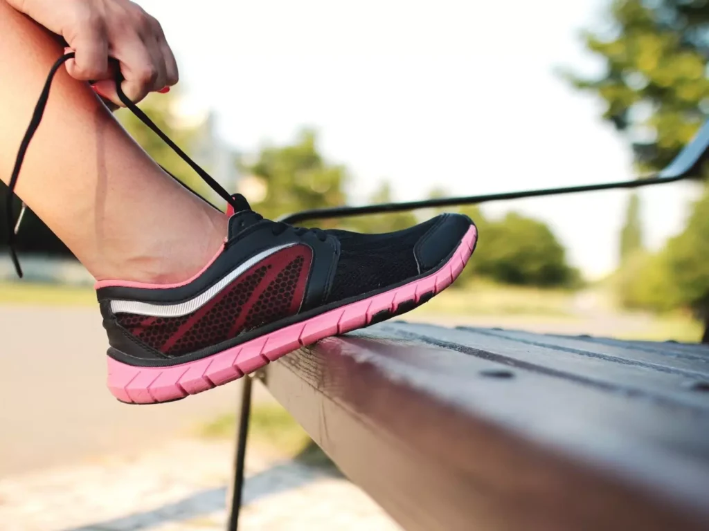 Person tying running shoe on track at sunset.