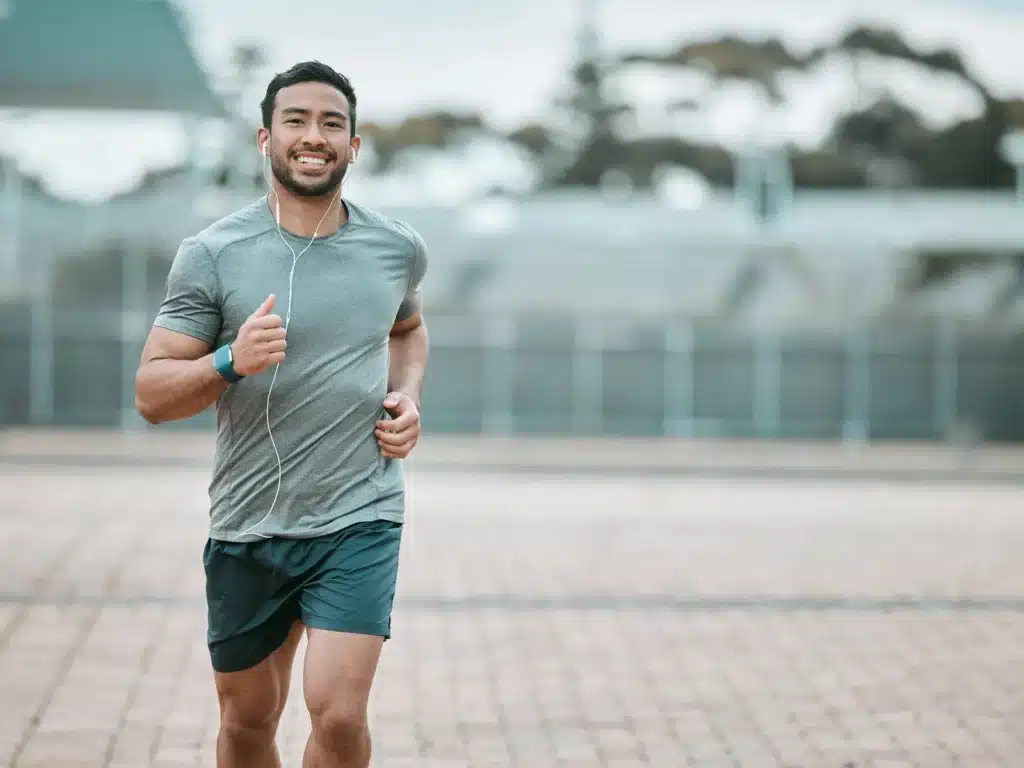 Man jogging outdoors with earphones and fitness tracker.
