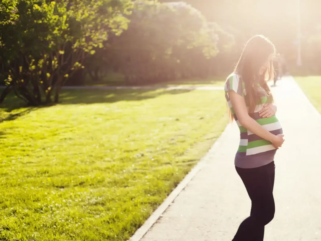 A women standing in a garden and looking at her baby bump.
